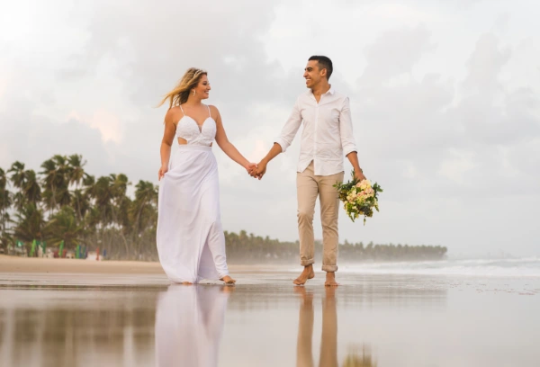 a married couple in beach wedding attire walking on a beach