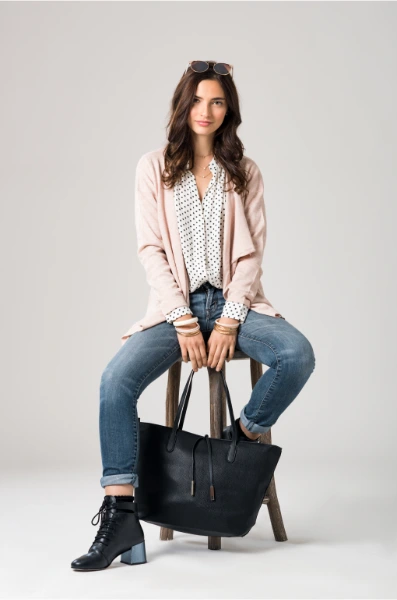 a brunette young woman sitting on a stool in a creme beige cardigan and blue jeans