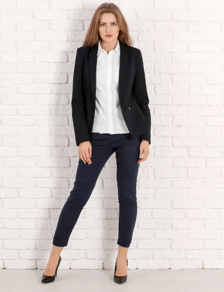 a red haired woman wears a black blazer, white shirt, black jeans and black high heels