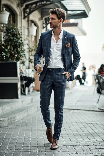 a man in a dark blue with light grey checkered suit walking on the street