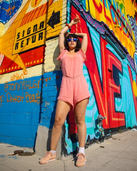 a young woman wearing a flatery orange jumpsuit. behind her is a wall with graffiti