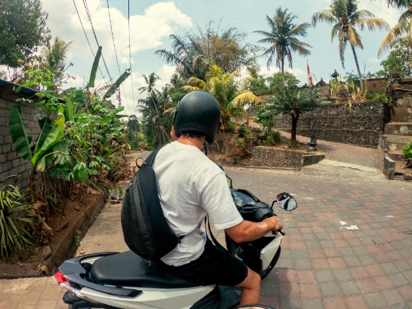 a young man sitting on a motor scooter riding on the streets of ubud