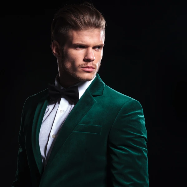 a young blonde man wears a black bow tie and a green velvet tuxedo