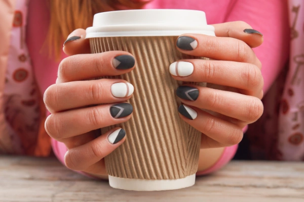 a woman holding a coffee in her hands with latte nails