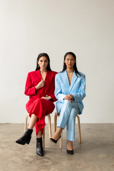 two young black haired woman wearing suits sitting on a chair