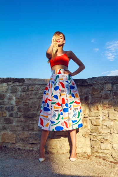 a young blonde woman wearing a red crop top and a floral midi skirt