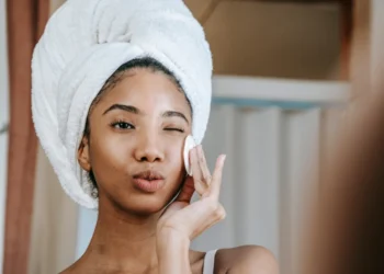a young woman with a white towel on her head cleansing her face for her nighttime skin care routine