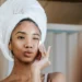 a young woman with a white towel on her head cleansing her face for her nighttime skin care routine