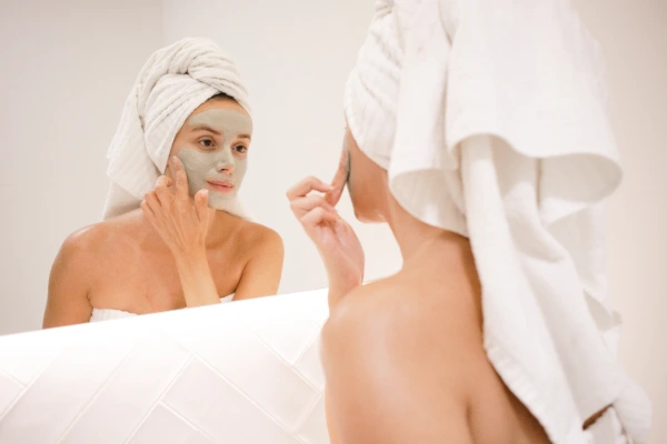 a young woman standing in front a mirror and putting on face mask on for her nighttime skin care routine