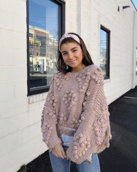 a young woman in a rose pom pom sweater standing on a parking lot