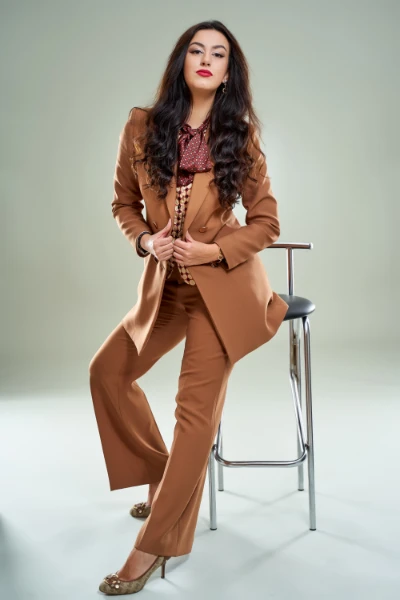 a young brunette woman sitting on a chair in a light brwon suit