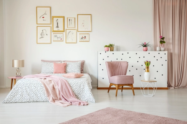 a feminin bed room with white and black dotted bed sheets and pink pillows. next to it is a pink chair