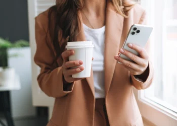 a woman with a cup and a phone wearing a business outfit