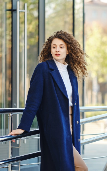 a woman with long curled hair in a dark blue wool coat